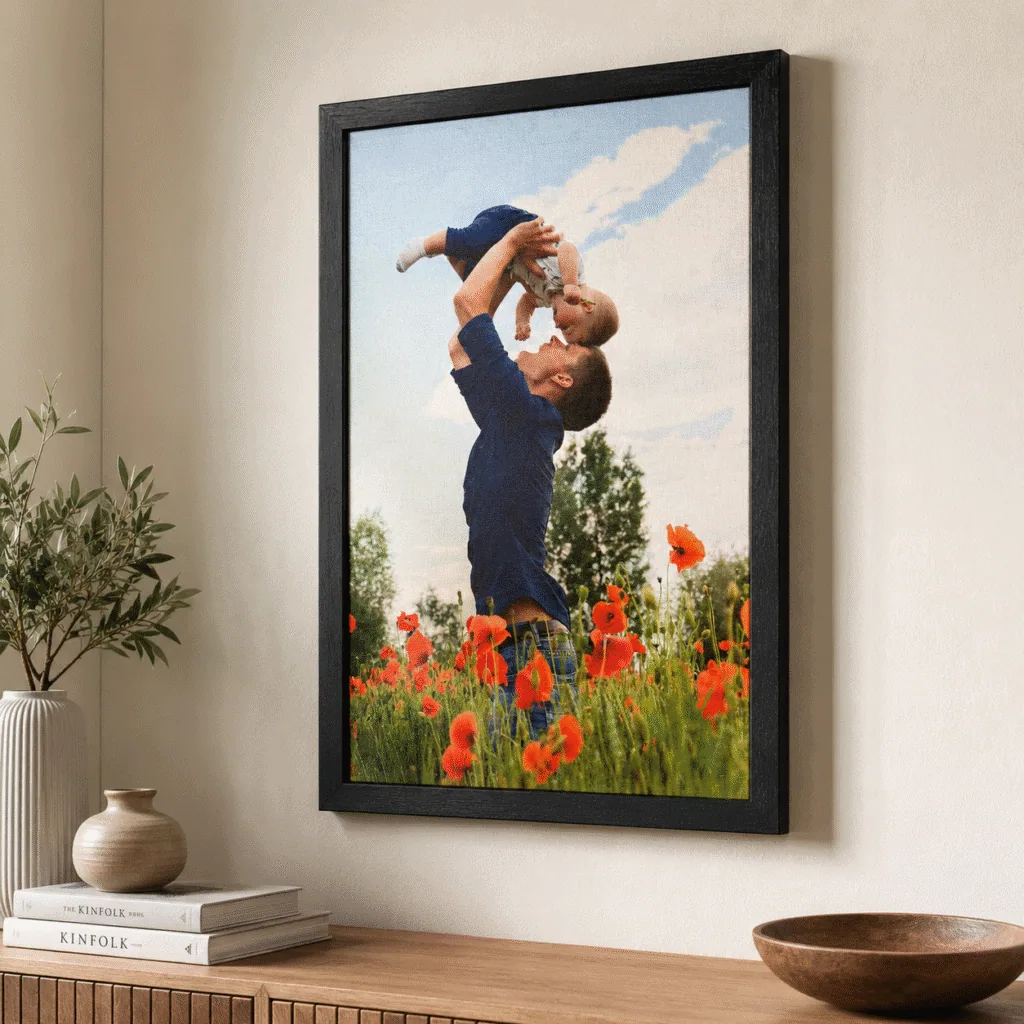 Cuadro tamaño 40x60 negro vertical, colgado en pared sobre mueble de madera, con foto de padre e hio en un campo de flores naranjas, con impresión en tela de Canva montada en Sintra, sin vidrio